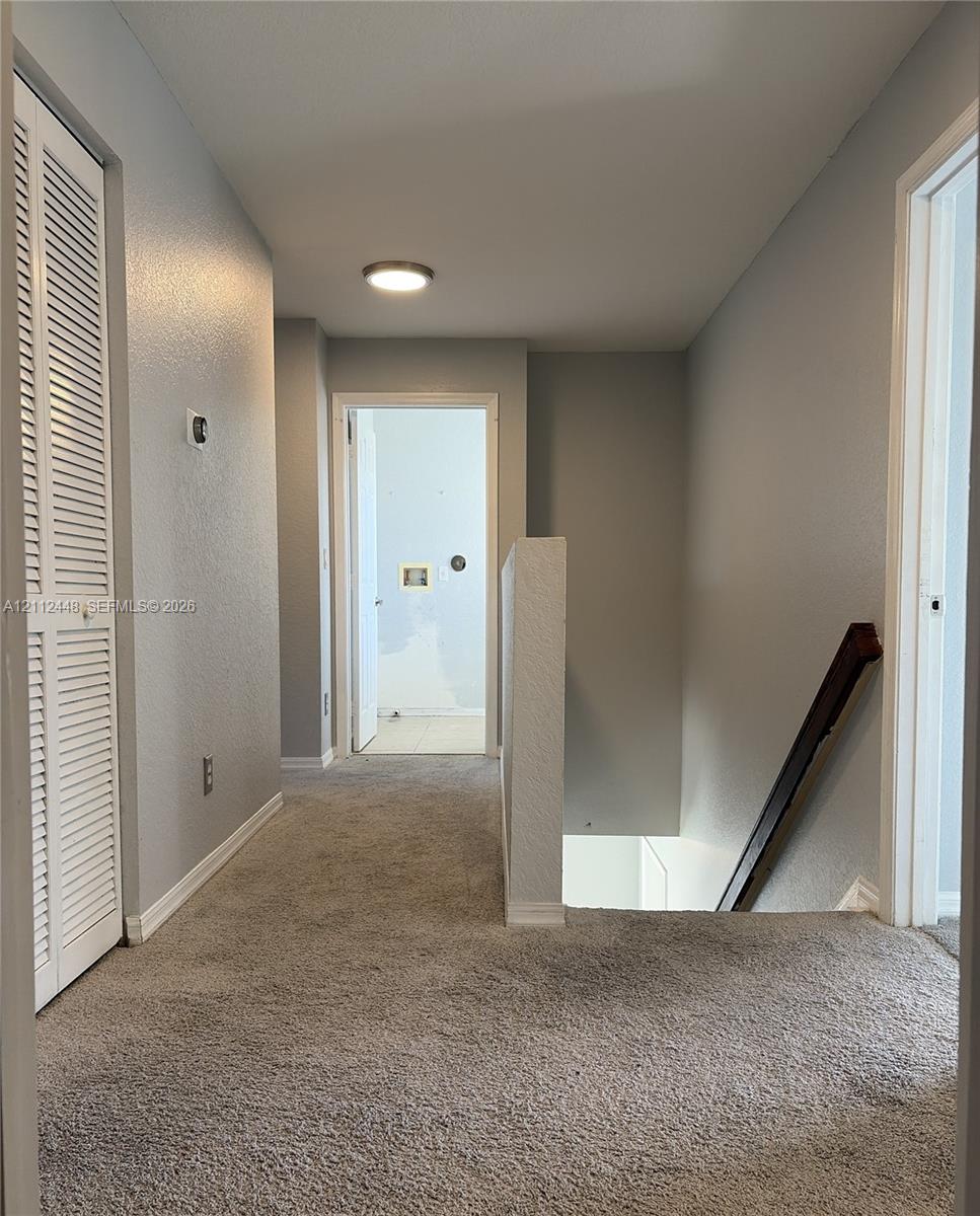 Hallway featuring neutral wall paint, carpeting, built-in louvered-door closet, and wooden staircase handrail