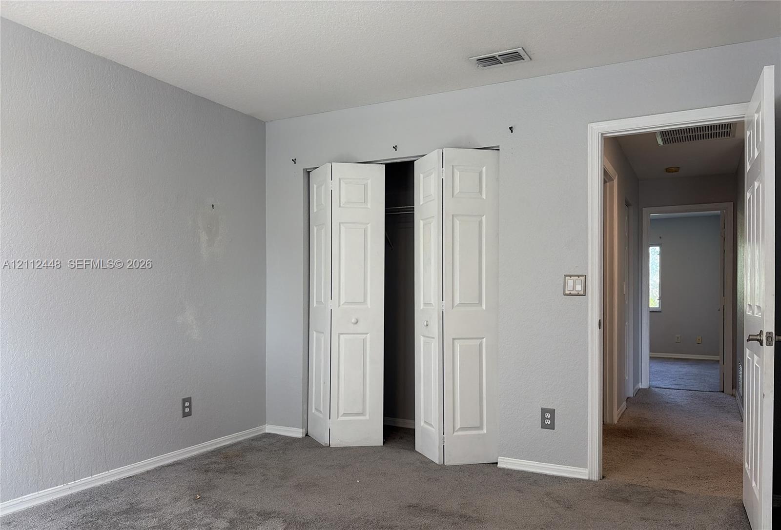Neutral-toned interior space featuring light grey walls, carpeted flooring, and a white six-panel bifold closet door
