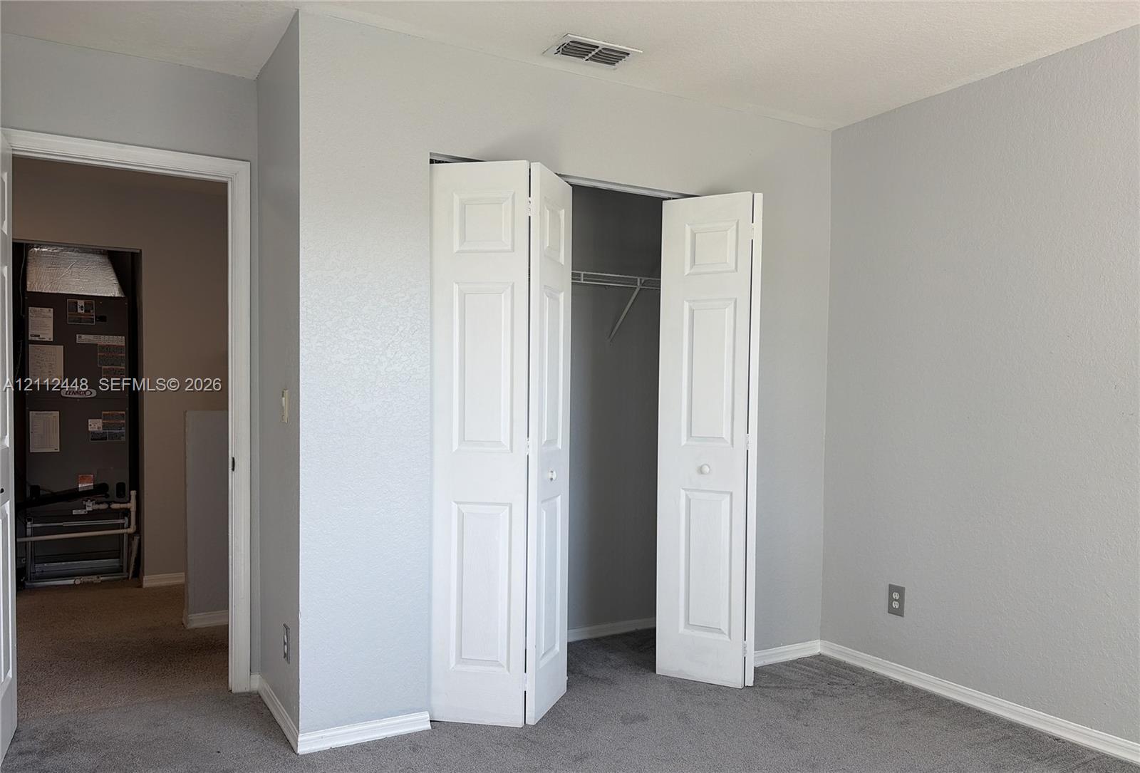 Neutral-toned walls paired with gray carpeting and a closet featuring white paneled bifold doors and built-in shelving