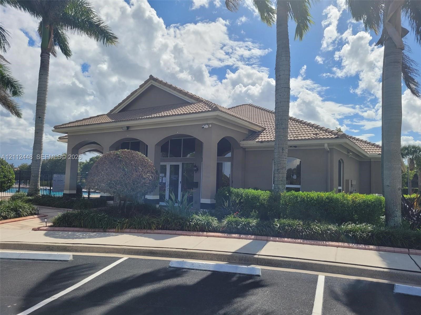 Stucco exterior featuring an arched entryway, tile roof, and landscaped garden beds