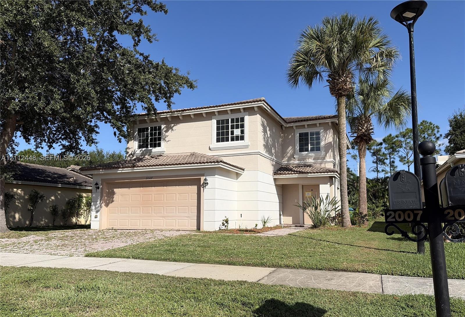 Two-story stucco exterior featuring a tiled roof, attached two-car garage, and mature palm trees