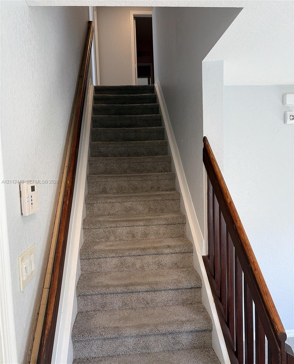 Staircase featuring neutral-toned carpeting, dark stained wood handrails, and vertical balusters