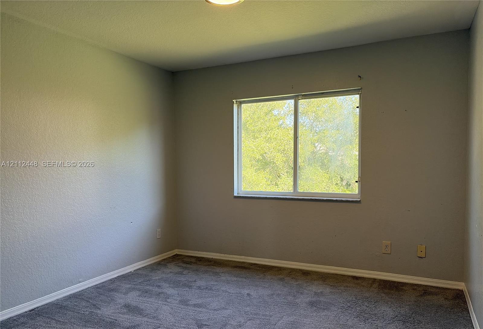 Interior room featuring neutral-toned walls, grey carpeting, and a sliding glass window