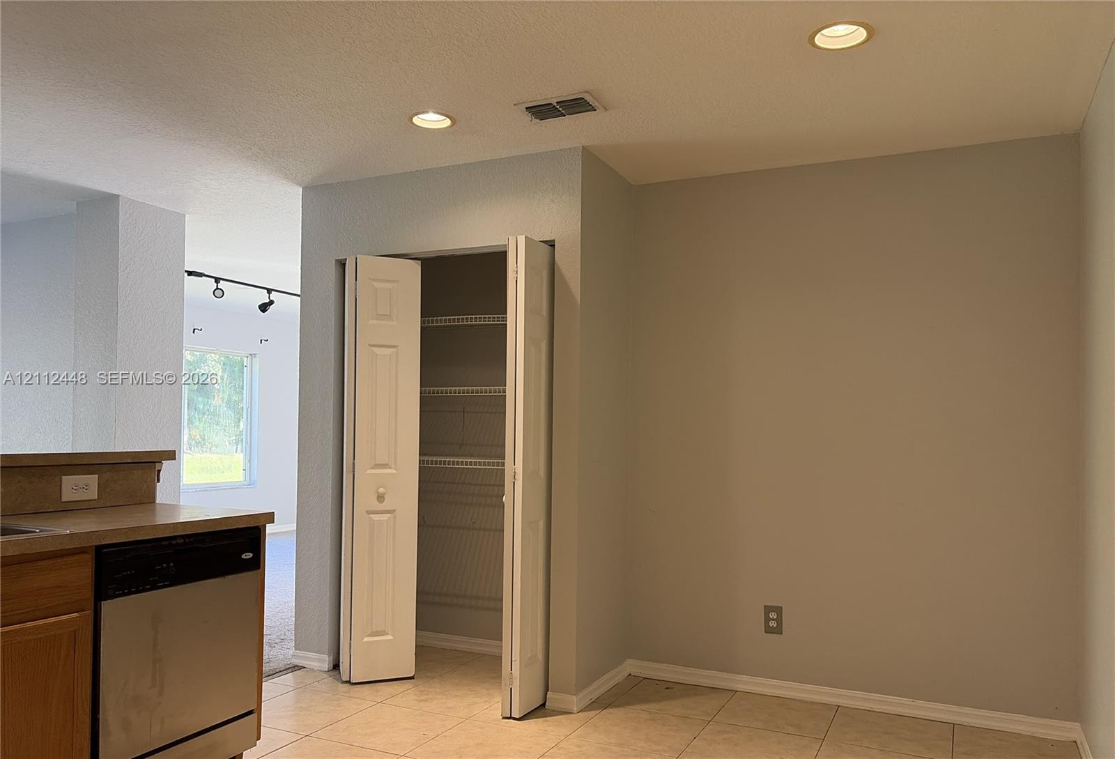 Ceramic tile flooring, built-in pantry with bi-fold doors and ventilated shelving, recessed ceiling lighting, and stainless steel dishwasher