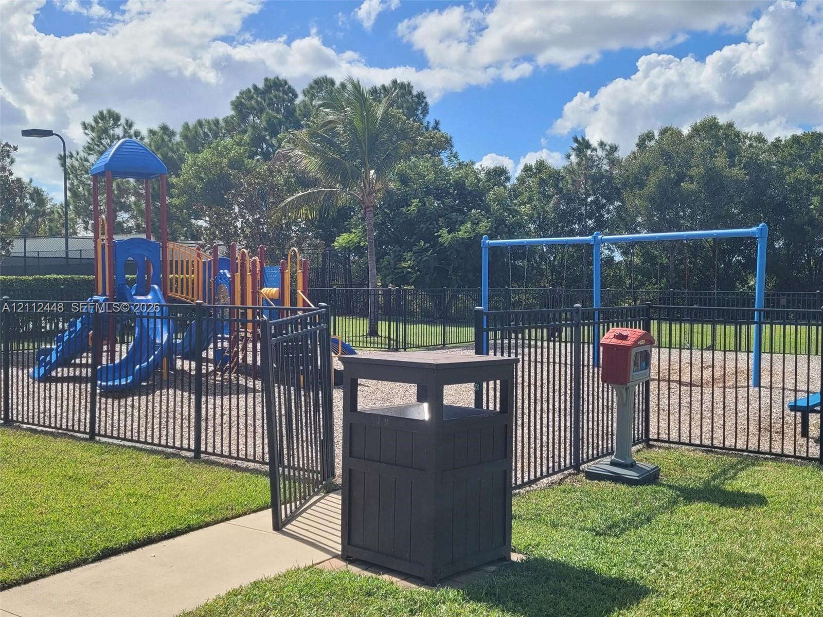Outdoor recreation area featuring a multi-component play structure, swing set, fenced perimeter, and gravel ground cover