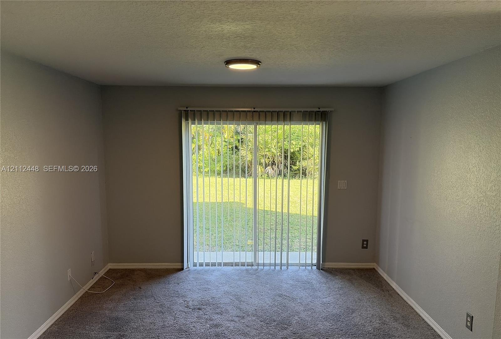 Interior space featuring textured walls, neutral wall-to-wall carpeting, and a glass sliding door with vertical blinds