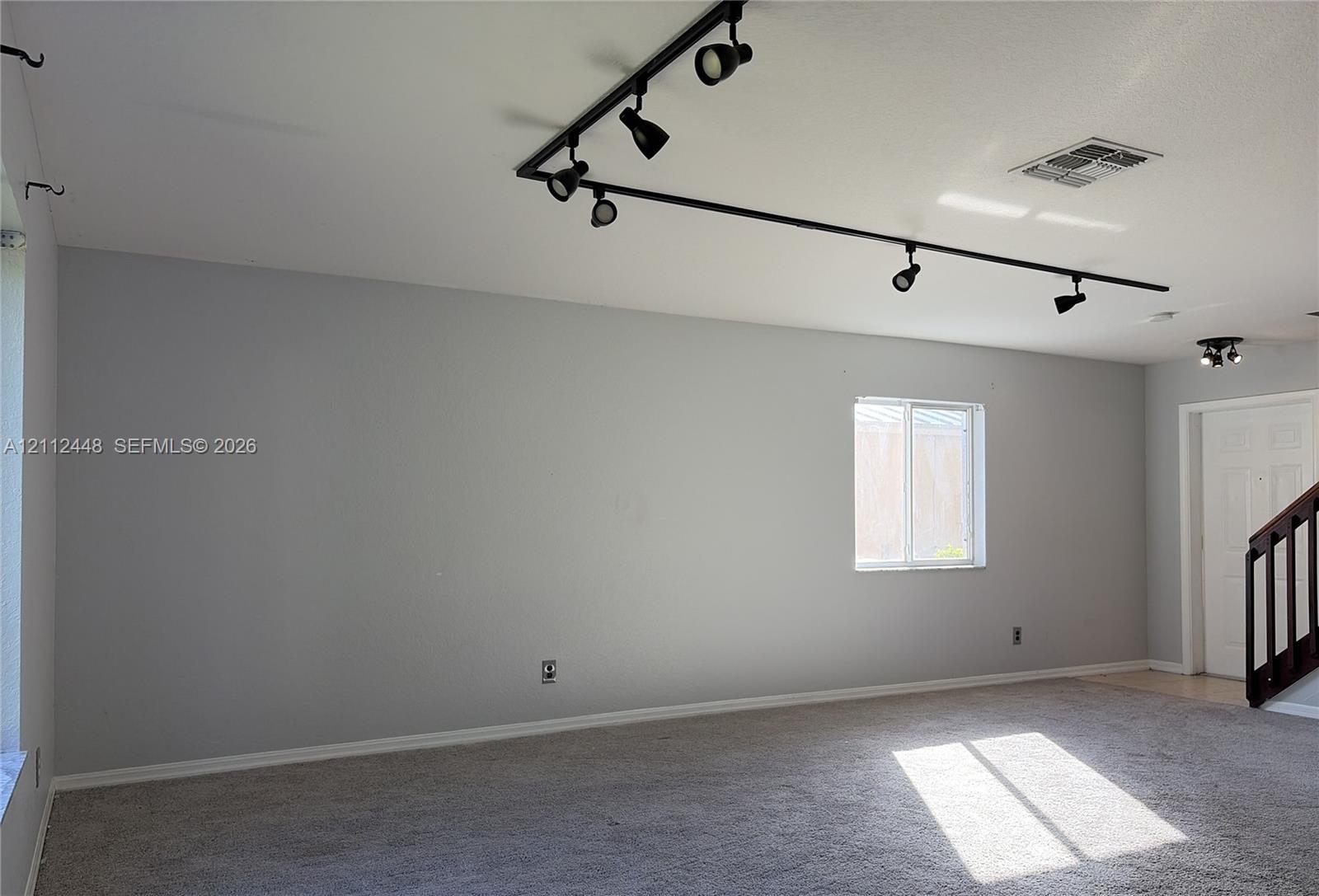 Interior space featuring wall-to-wall carpeting, adjustable black track lighting, and a multi-panel door with a dark-toned handrail