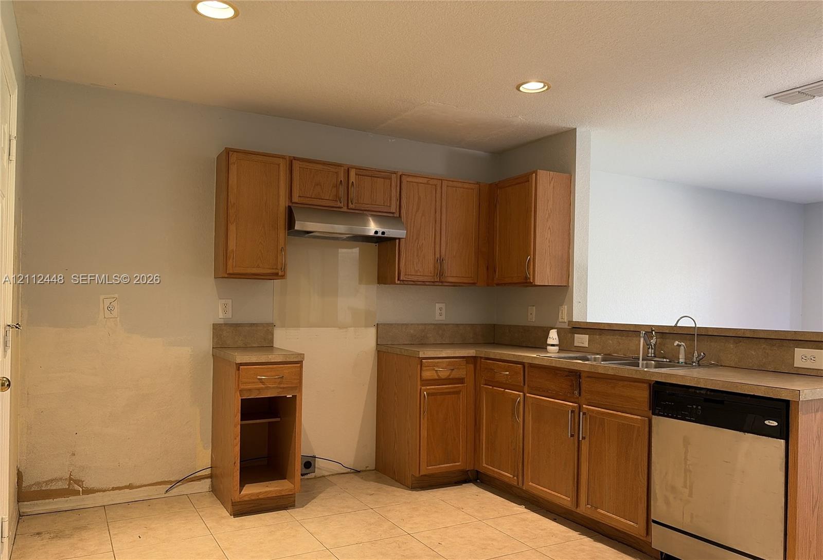 Kitchen featuring wood cabinetry, stainless steel range hood, stainless steel dishwasher, double basin sink, and tile flooring