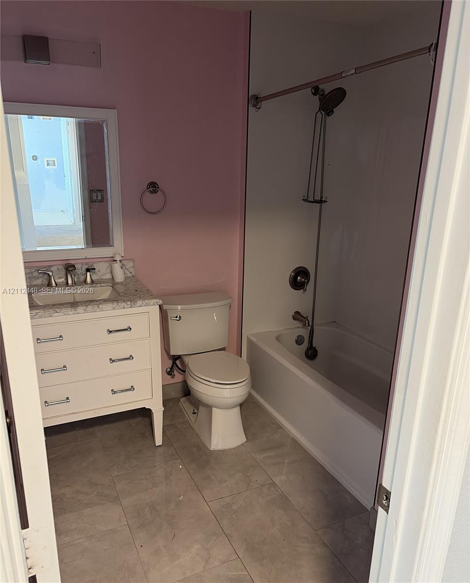 Bathroom featuring a vanity with a stone-finish countertop, undermount sink, ceramic tile flooring, and a shower-tub combination with a wall-mounted fixture