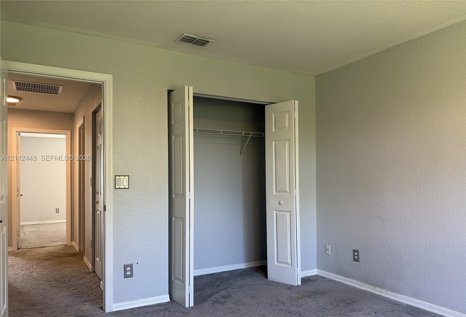Neutral-toned interior walls featuring a built-in closet with bifold doors and integrated wire shelving, complemented by carpeting