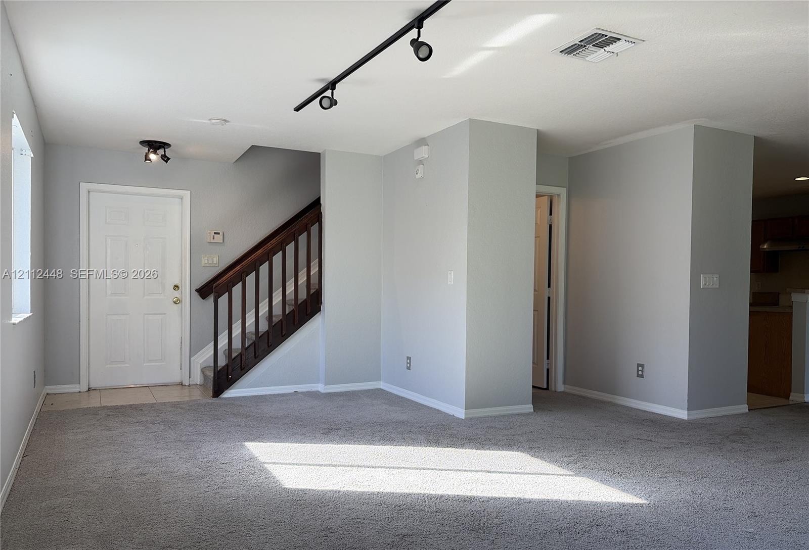 Interior space featuring neutral-toned wall paint, neutral carpeting, track lighting, and a staircase with a dark wood railing
