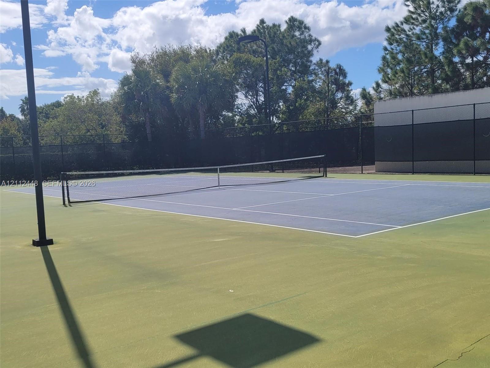 Tennis court featuring a hard surface, perimeter chain-link fencing, and overhead court lighting