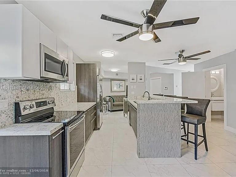 Kitchen featuring custom cabinetry, speckled stone countertops, stainless steel appliances, a kitchen island with stone finish, and tile flooring