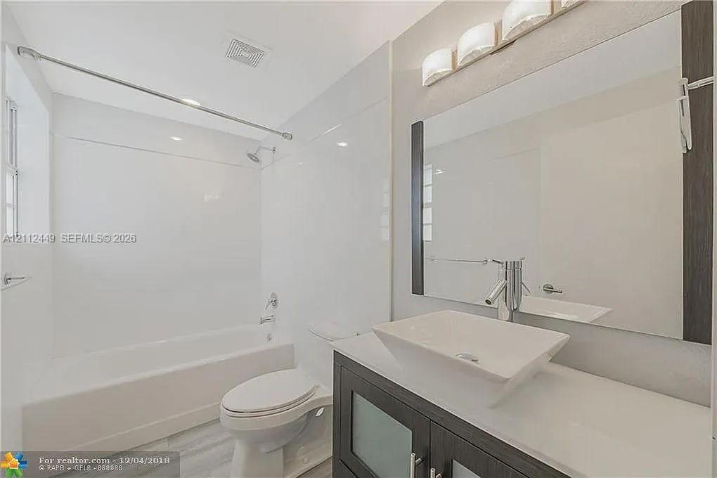 Dark wood-finish vanity with a rectangular vessel sink, topped by a sleek polished faucet, set against a large wall-mounted mirror with integrated lighting