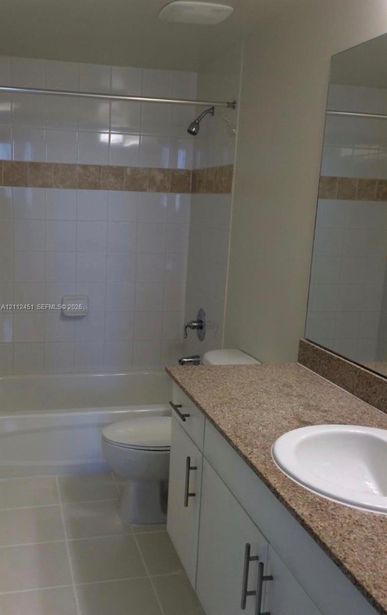 Bathroom featuring a vanity with stone-finish countertop, white cabinetry with metallic hardware, integrated sink, and a shower-tub combination with tiled walls and decorative accent band