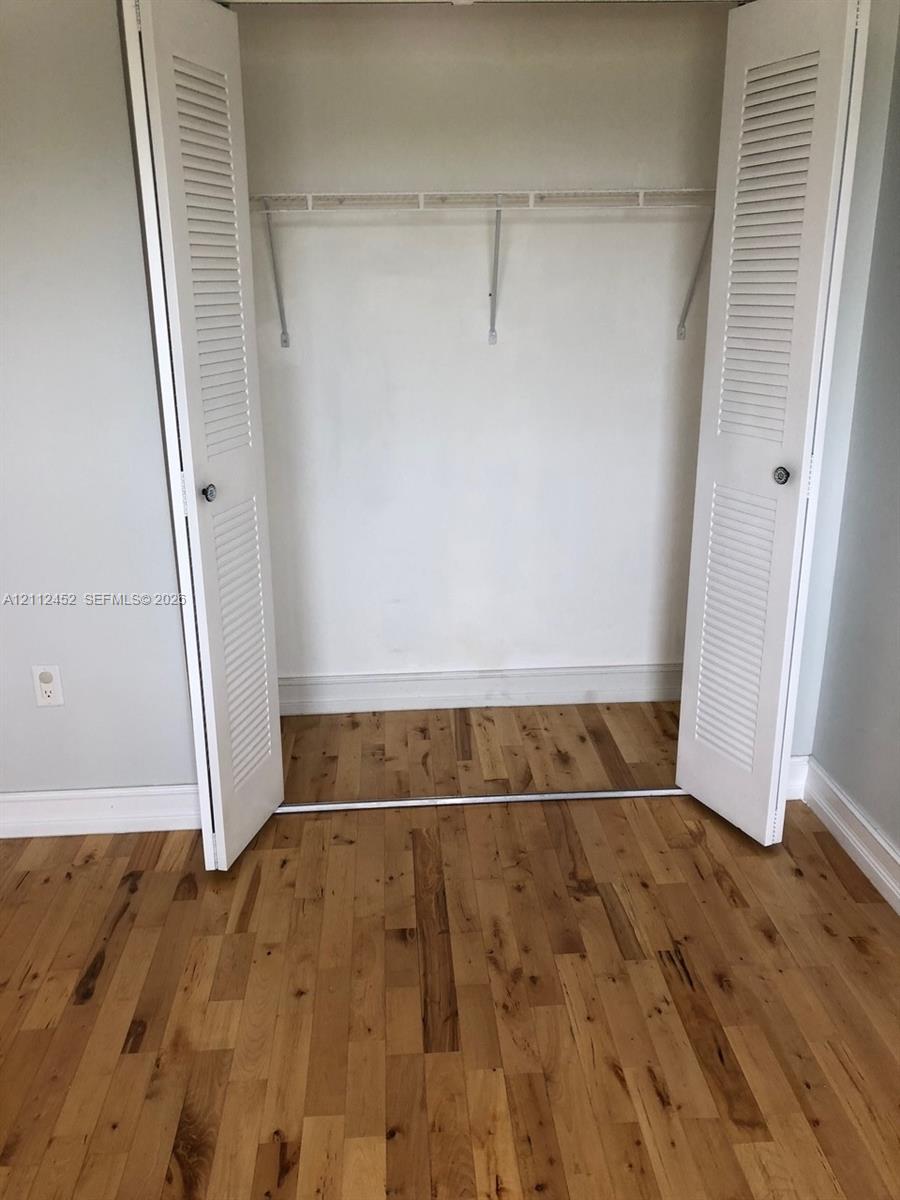 Closet featuring white louvered bifold doors and a metal shelving rod, set against wood-finish flooring
