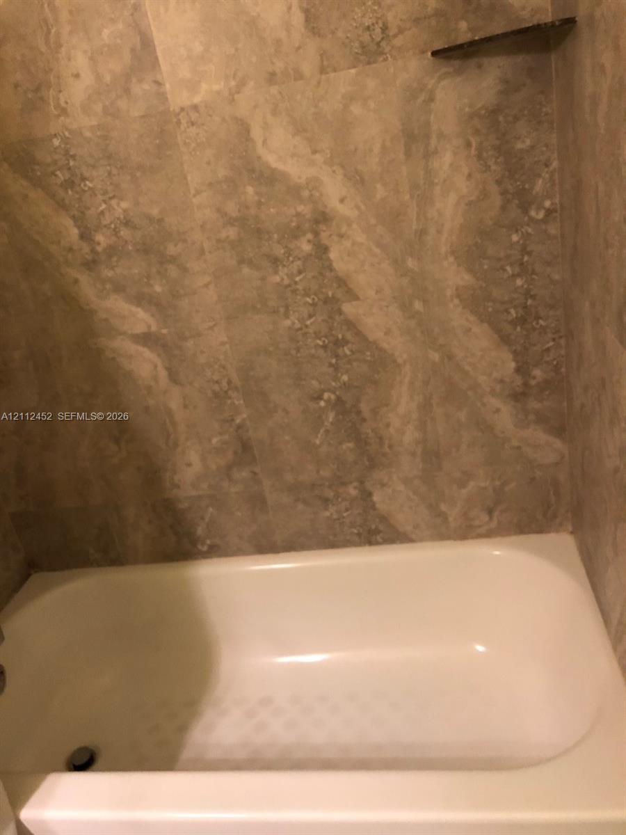 Bathtub with a white finish, surrounded by floor-to-ceiling large-format stone-finish wall tiles and a built-in triangular corner shelf