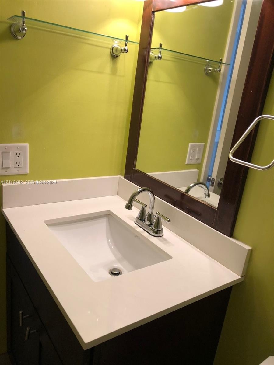 Dark wood-finish vanity with a white countertop and undermount sink, chrome faucet, framed mirror, and mounted glass shelving