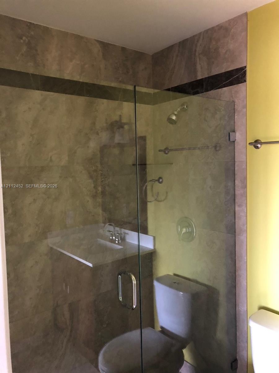Walk-in shower enclosure with glass door, stone-tile surround, integrated accent border, chrome rainfall showerhead, and wall-mounted metal hardware
