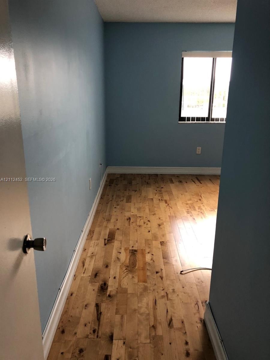 Room featuring wood-finish flooring, a single window, and solid interior door with a brushed metal handle
