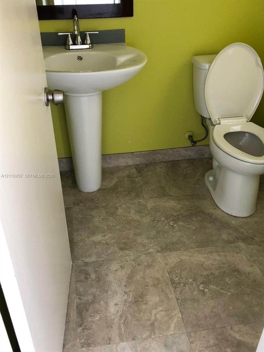 White pedestal sink with chrome faucet, stone-finish tile flooring, and a two-piece porcelain toilet White pedestal sink with chrome faucet, stone-finish tile flooring, and a two-piece porcelain toilet