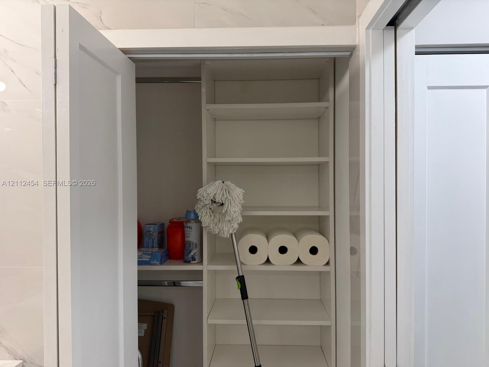 Built-in storage closet featuring white shelving, a clothing rod, and dual-swing doors