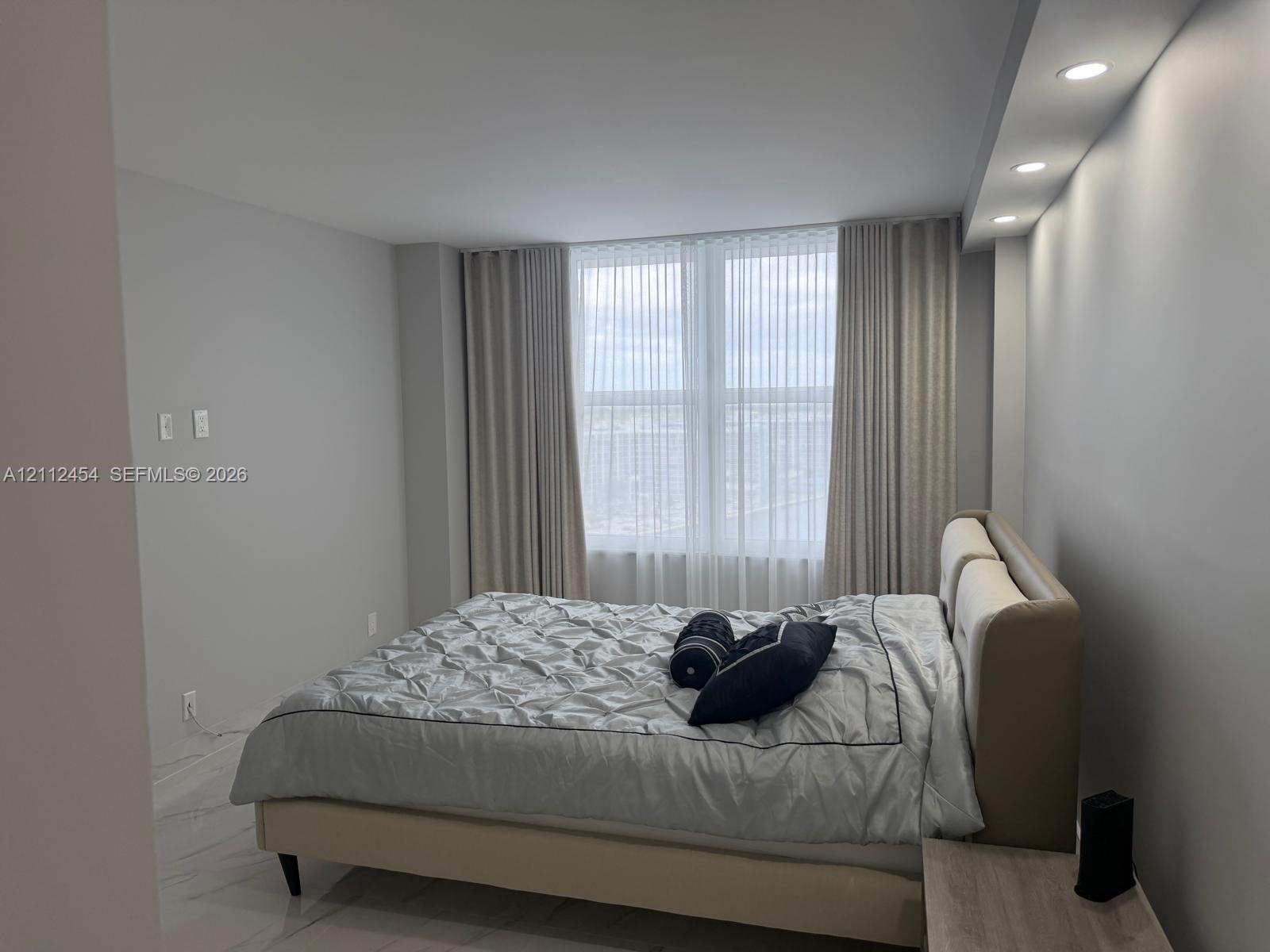Large windows with floor-to-ceiling drapery, recessed soffit lighting, and high-gloss tile flooring