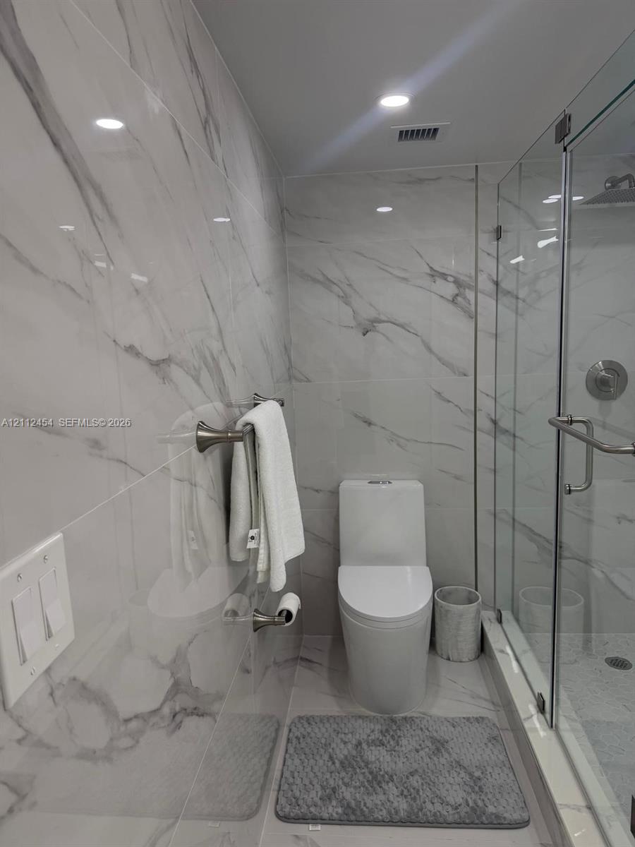 Full-height, stone-finish wall tiling, glass-enclosed shower stall with polished metal fixtures, and dual-flush toilet