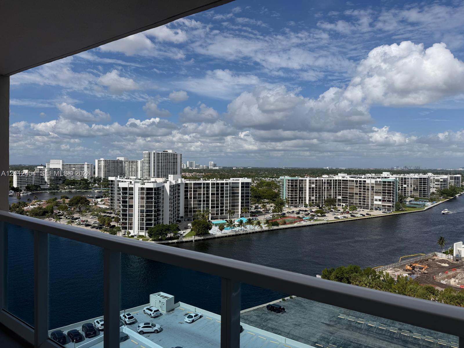 Covered balcony with a white metal railing overlooking a waterway and high-rise skyline