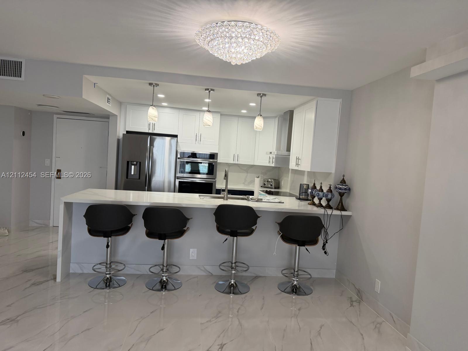 Kitchen featuring white cabinetry, a waterfall-edge stone countertop, stainless steel built-in double wall oven, pendant lighting, and stone-finish flooring