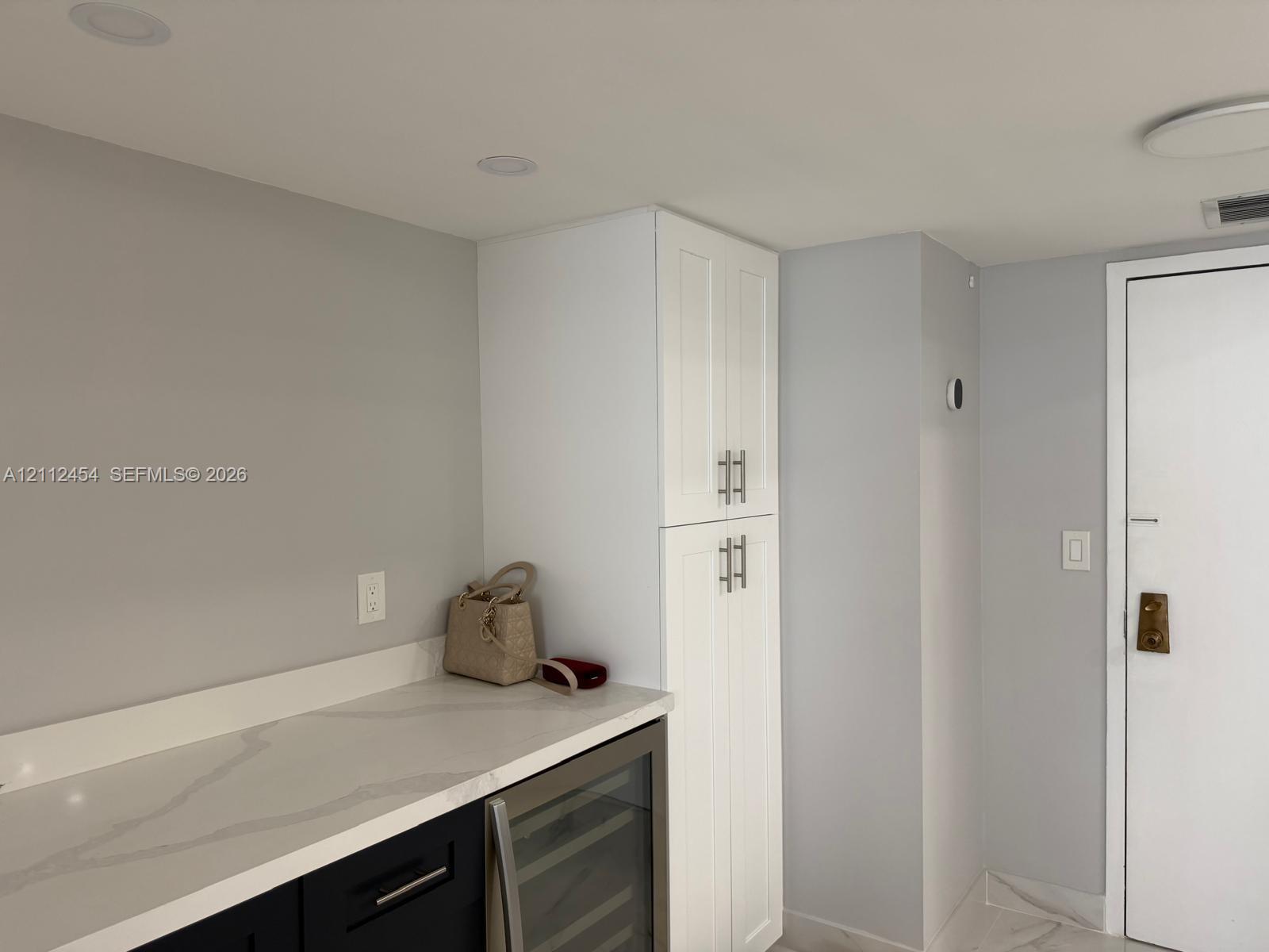 Custom cabinetry featuring white shaker-style pantry storage, black lower cabinets, stone-finish countertops, and an integrated wine refrigerator