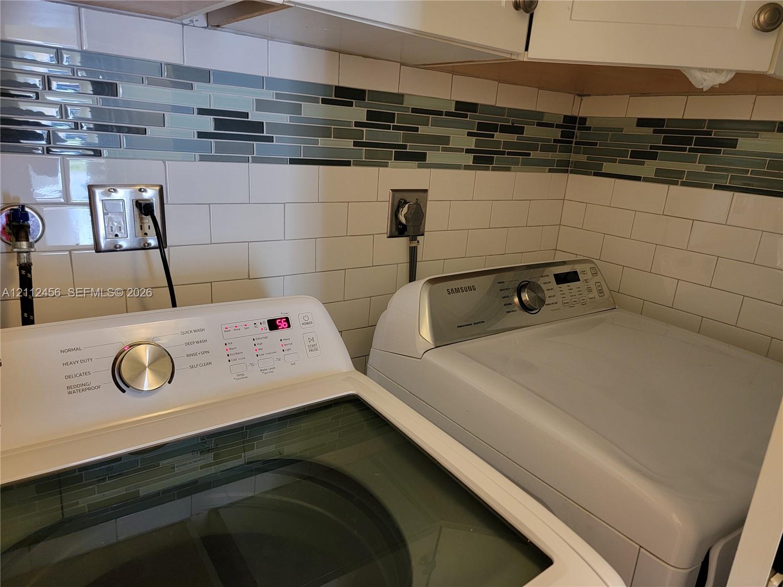 Subway tile backsplash featuring a decorative linear glass accent border, white cabinetry, and integrated laundry appliances