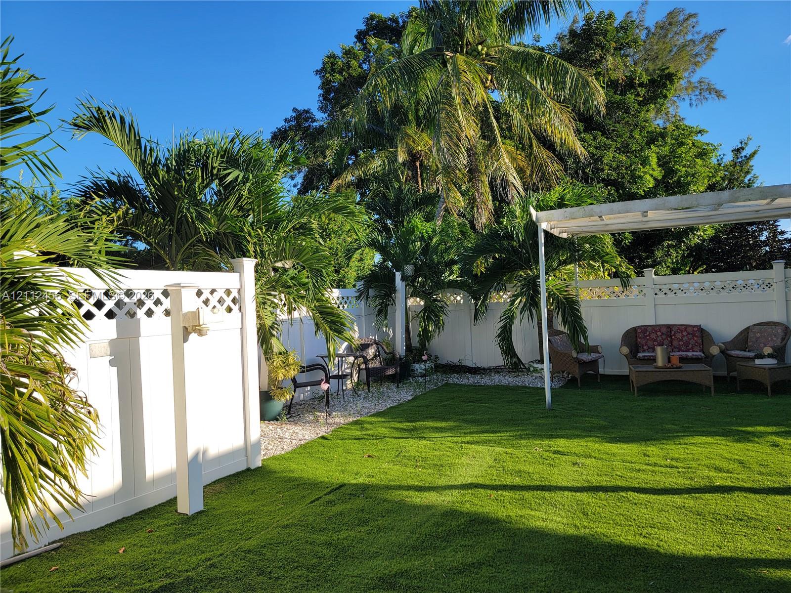 Private backyard featuring a manicured lawn, white vinyl fencing with lattice detailing, and a detached pergola
