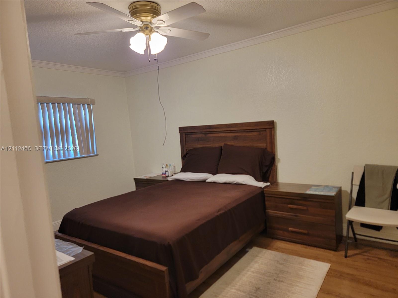 Room featuring wood-finish flooring, crown molding, and a ceiling fan with integrated lighting