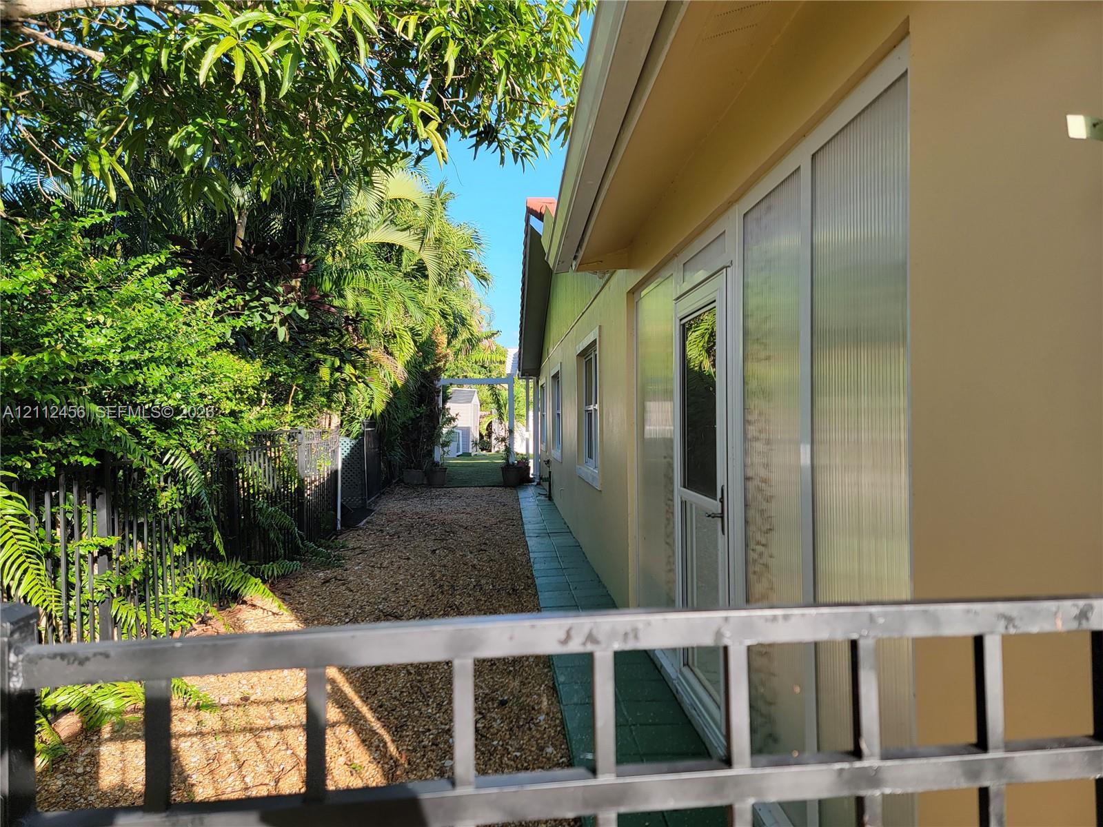 Exterior side yard featuring metal perimeter fencing, gravel ground cover, and a paved walkway along the side of the structure