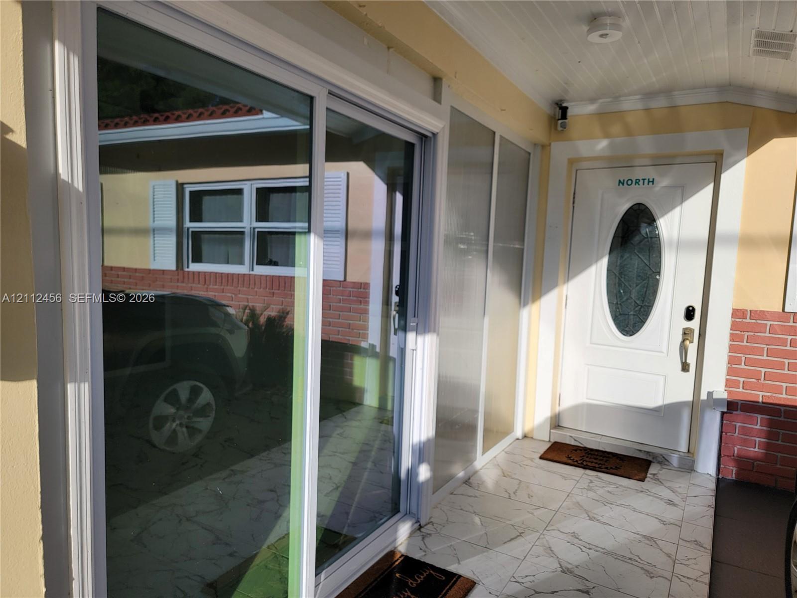 Covered entryway featuring stone-finish floor tile, a white entry door with an oval glass insert, and full-length glass sliding doors