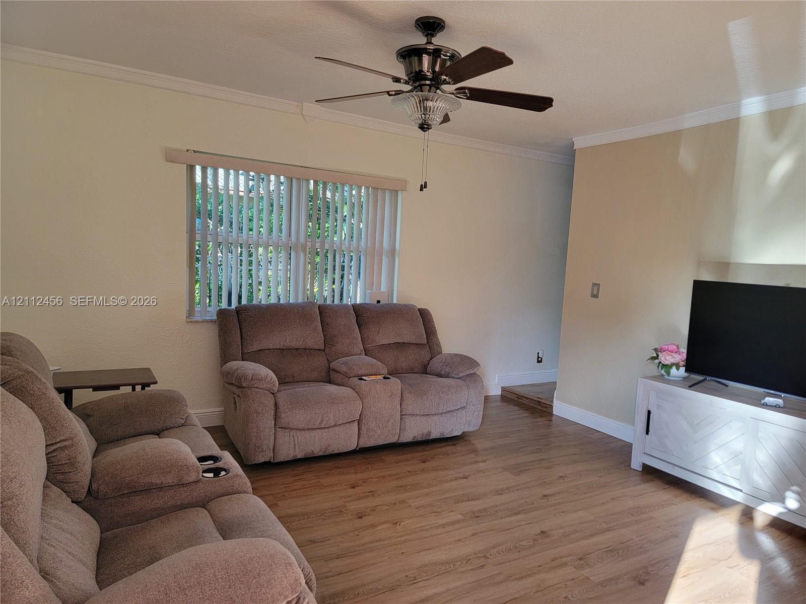 Room featuring wood-finish flooring, crown molding, a multi-blade ceiling fan with integrated lighting, and vertical window blinds