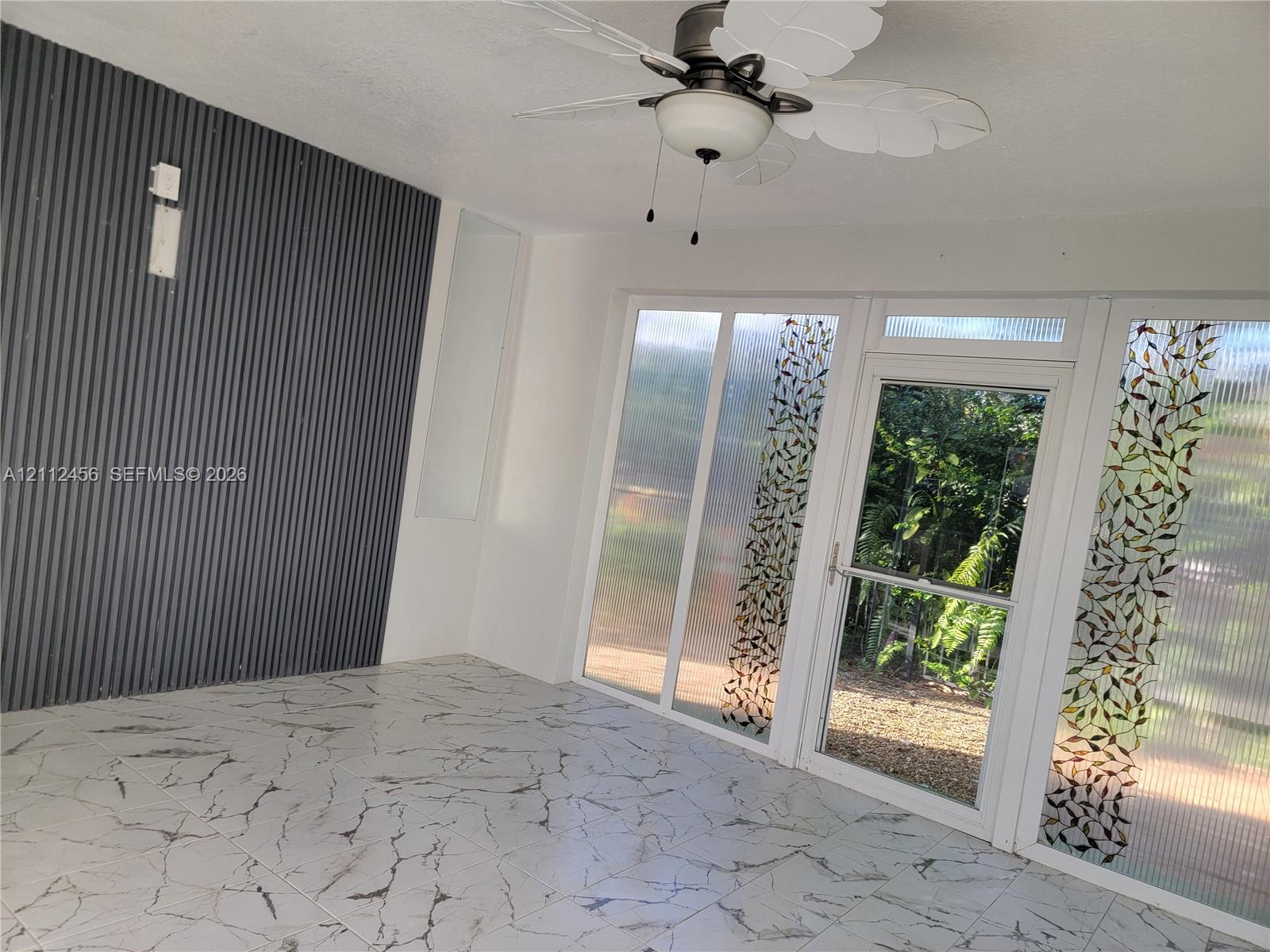 Enclosed space featuring large-format tile flooring, a corrugated metal accent wall, and a ceiling fan with leaf-patterned blades