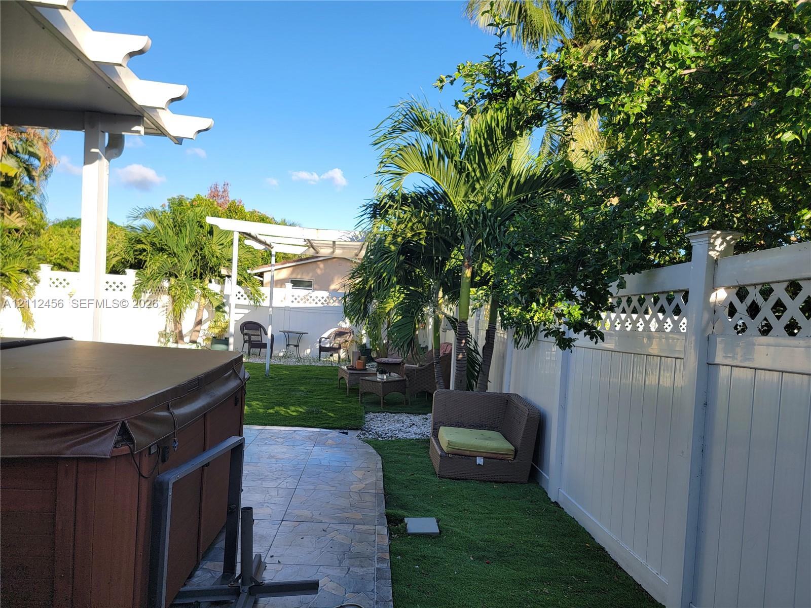 Backyard featuring a paved patio, covered pergola, vinyl privacy fencing with lattice detail, and established palm trees