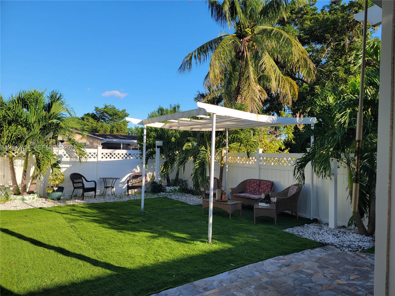 Rear yard featuring a white lattice-top privacy fence, synthetic turf lawn, white pergola, and stone paver patio