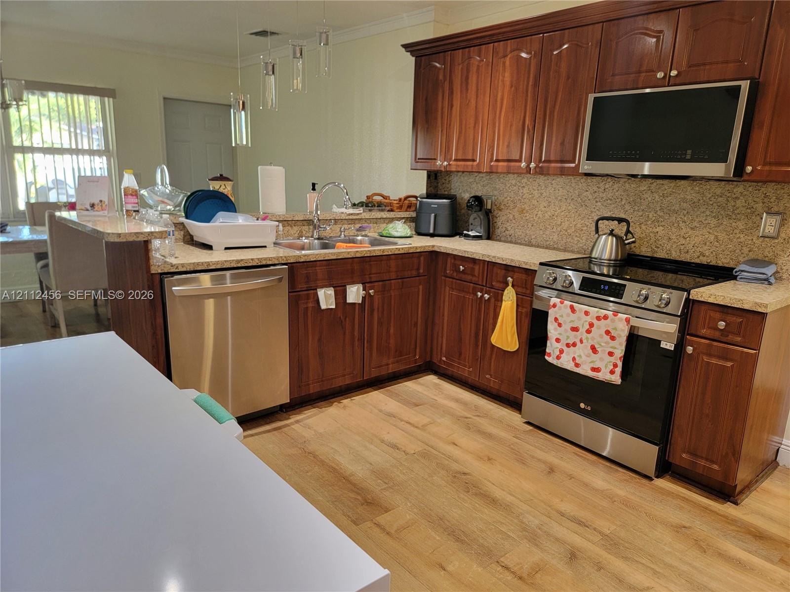 Kitchen featuring stained wood cabinetry, stone-finish countertops, stainless steel appliances, a peninsula with a stainless steel sink, and wood-finish flooring