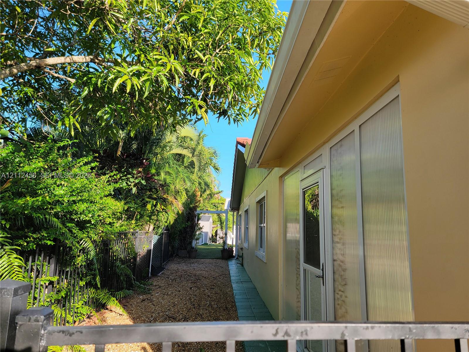 Exterior side yard featuring a paved walkway, gravel ground cover, privacy fencing, and mature vegetation