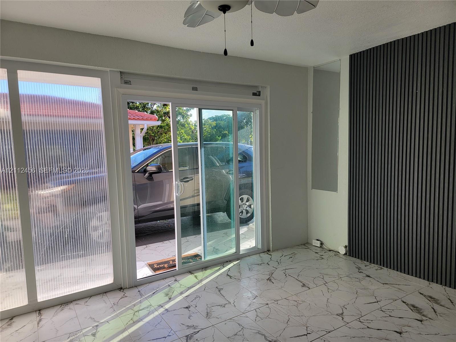 Interior space featuring large-format marbled floor tile, a dark wood-slat accent wall, sliding glass doors, and a ceiling-mounted fan