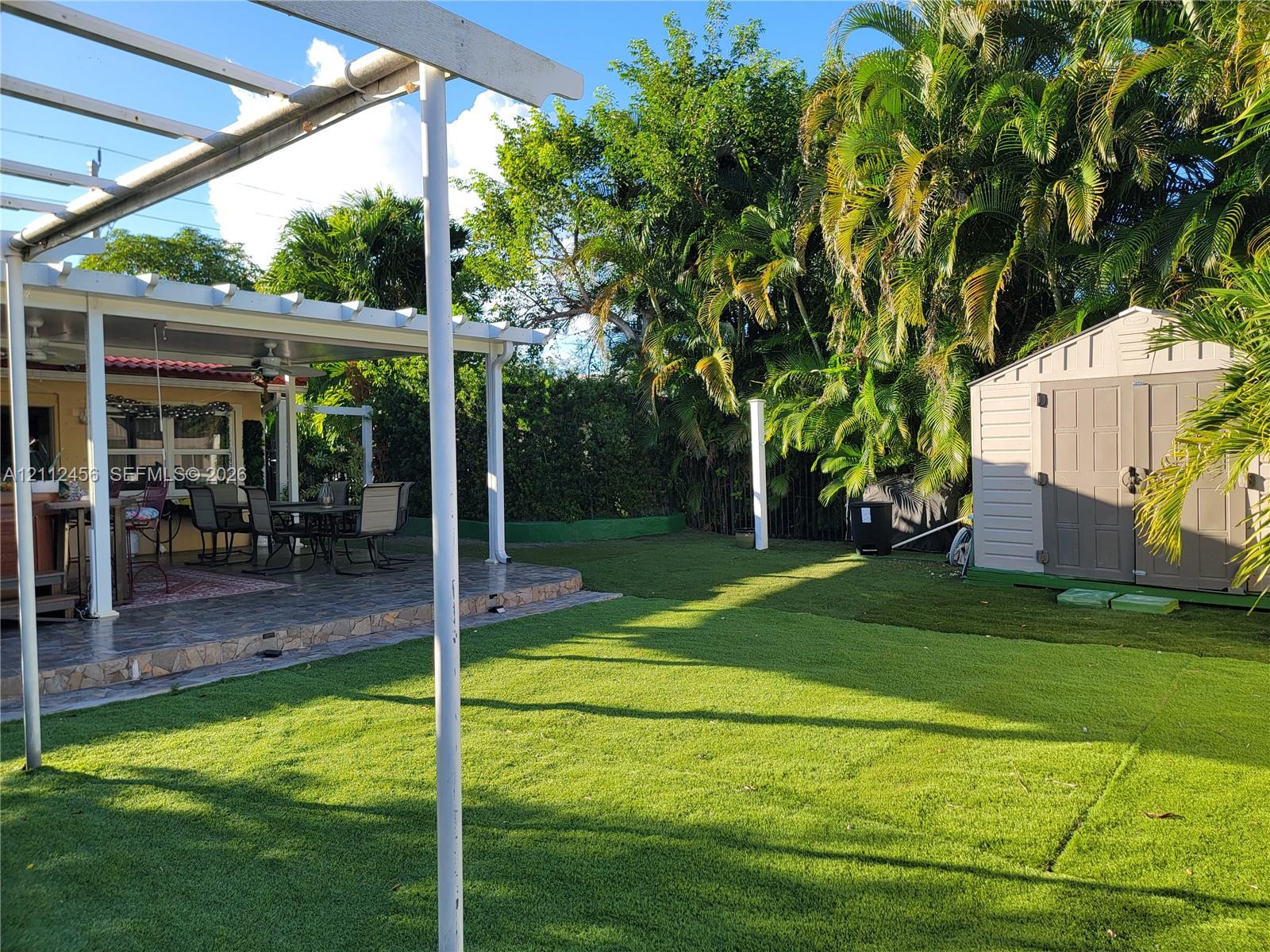Rear exterior space featuring a covered patio with a white pergola, a lawn area, and a detached storage shed