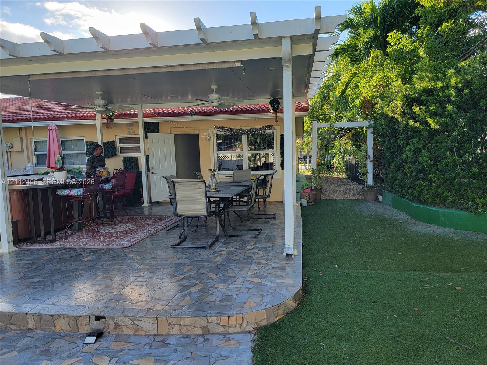 Covered patio featuring a solid-surface roof structure, ceiling fans, stone-finish tile flooring, and a pergola perimeter