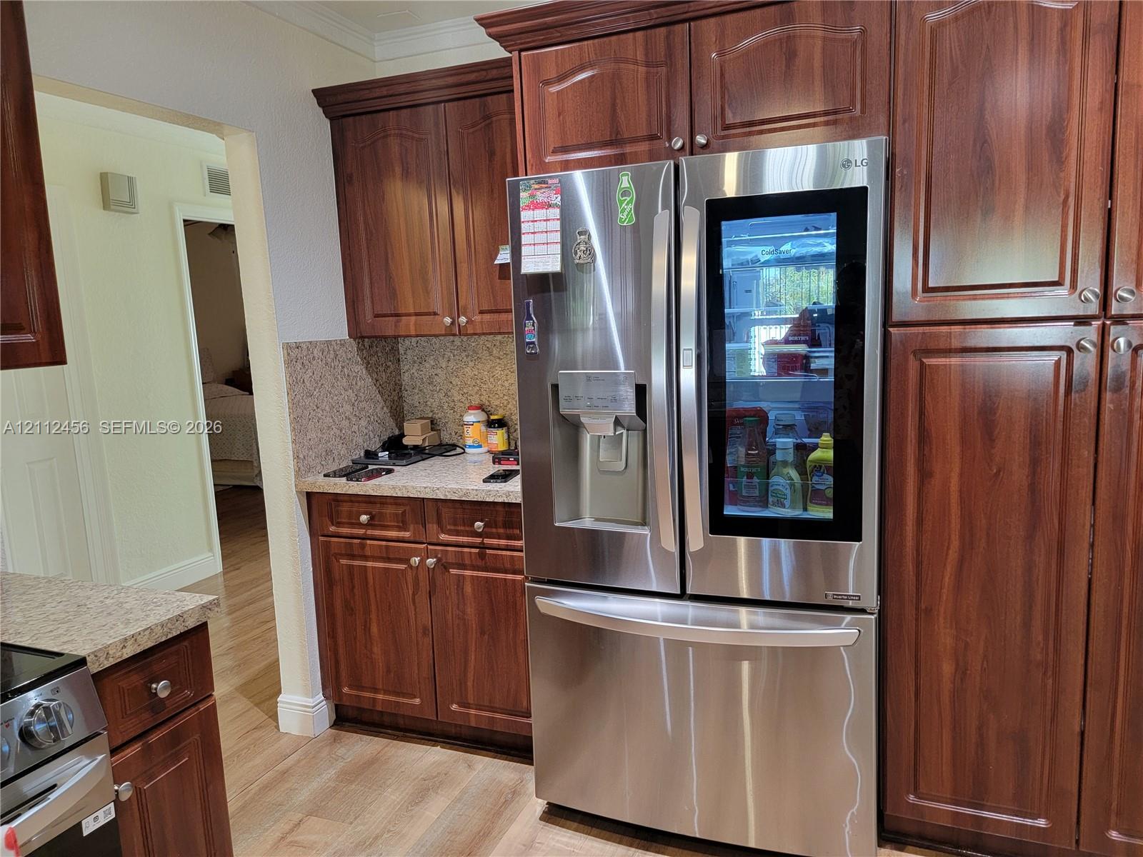 Stained wood cabinetry, stone-texture countertops, and stainless steel French door refrigerator with glass-panel door