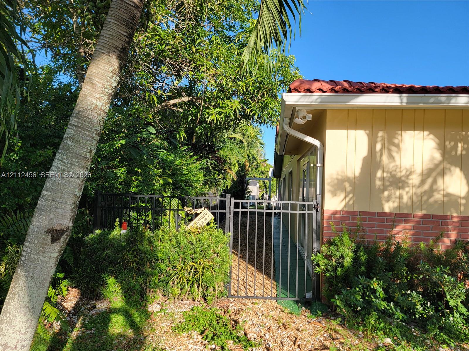 Exterior featuring tile roofing, vertical panel siding, lower brick masonry, and a metal gate enclosing the side yard