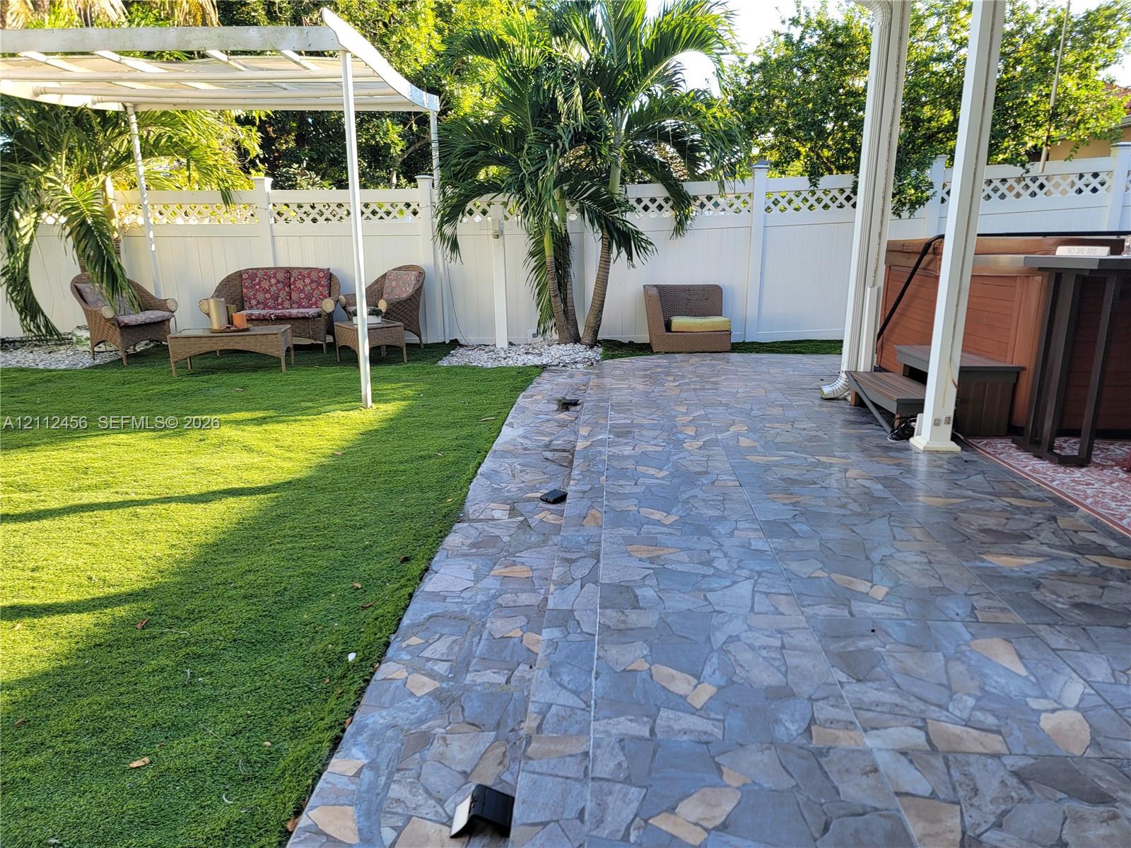 Private backyard featuring a flagstone patio, custom white lattice-topped fencing, a built-in pergola, and an integrated hot tub