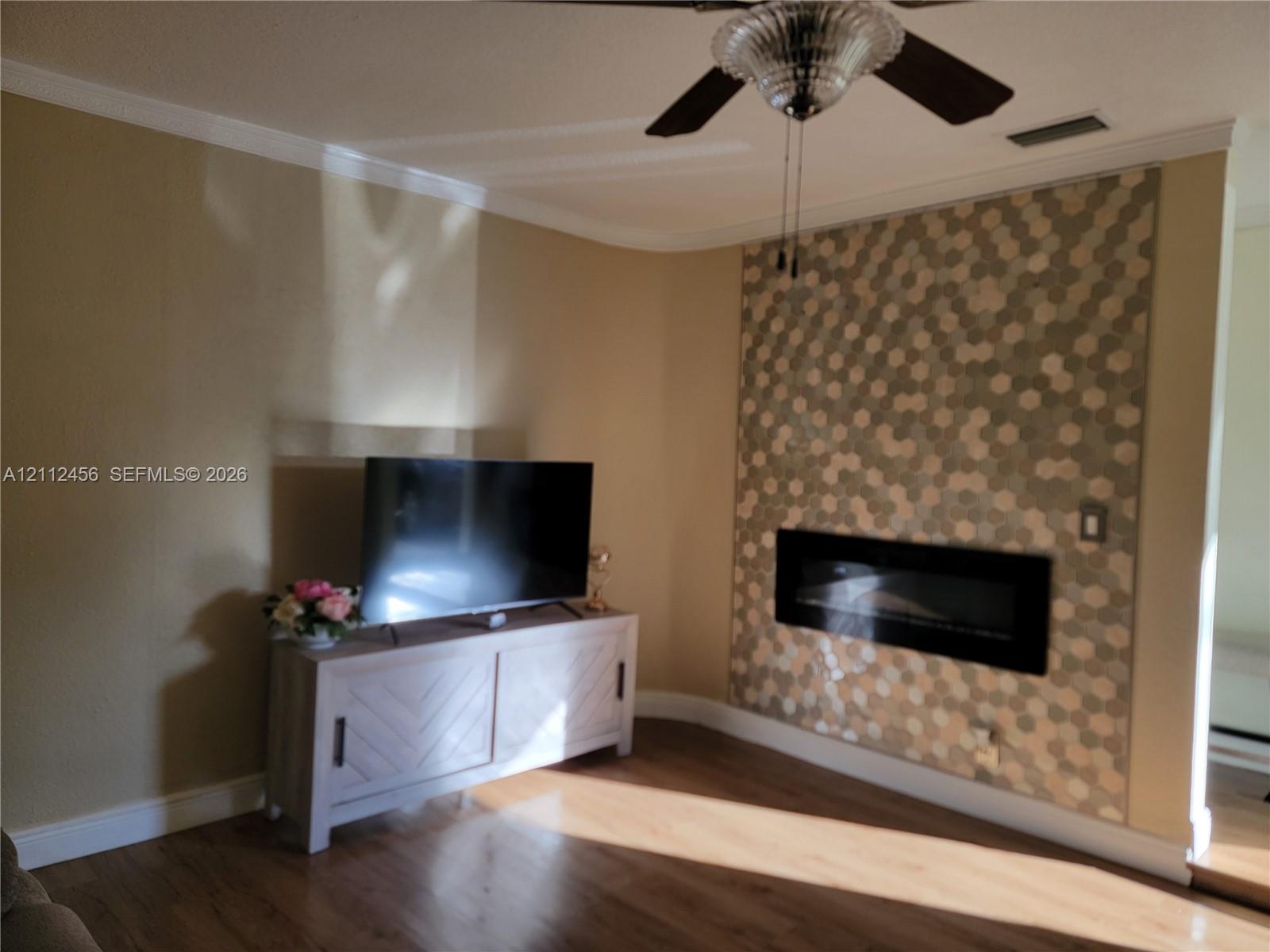 Living area featuring wood-finish flooring, a wall-mounted electric fireplace, and a decorative hexagonal tile accent wall