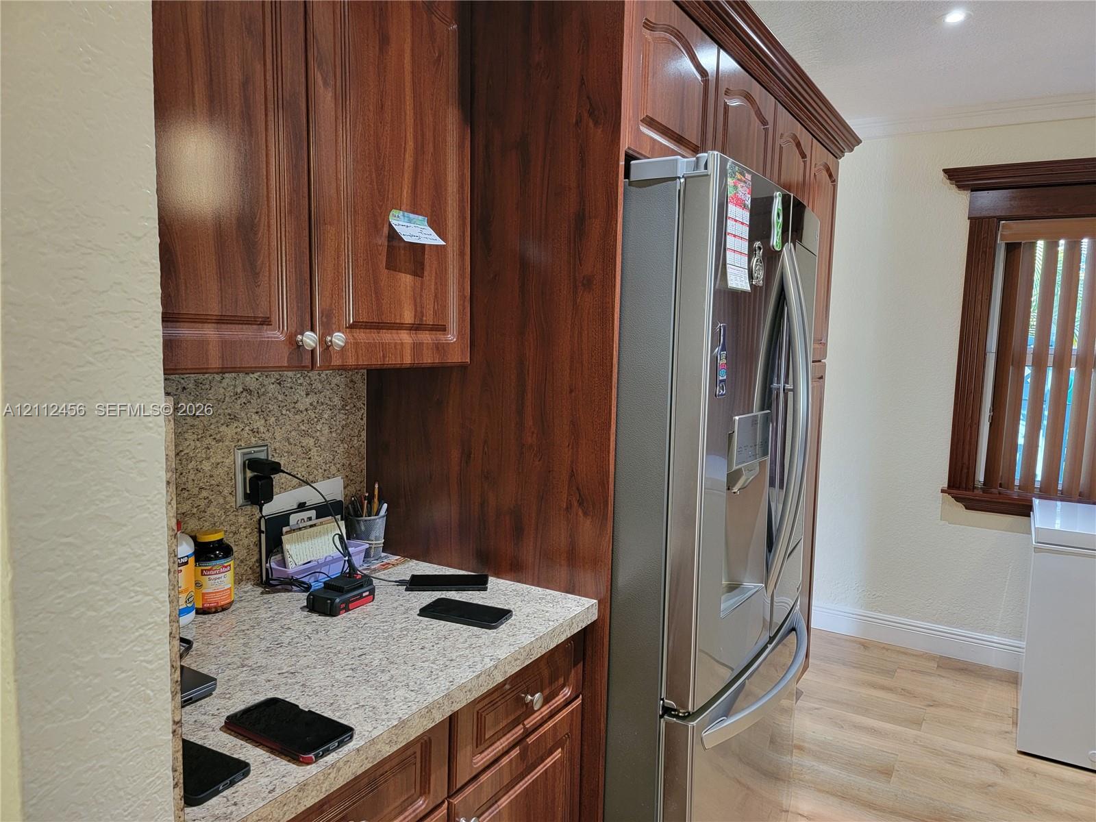 Kitchen cabinetry featuring dark wood-finish, stone-patterned countertops, a stainless steel refrigerator, and wood-finish flooring